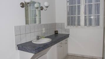 A bathroom with a white sink, granite countertop, and a window with a white curtain.