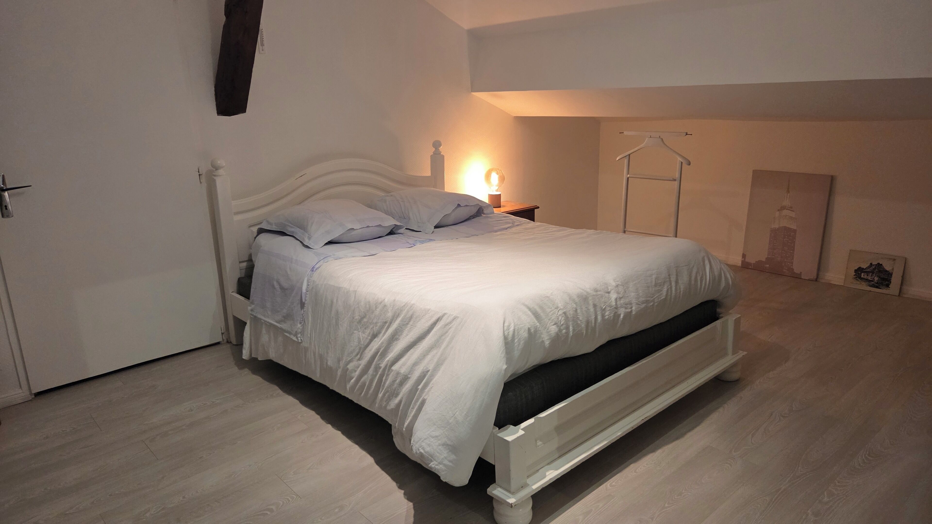 A bedroom with a bed, bedside table, lamp, and wall art.