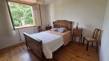 Une chambre à coucher avec un lit en bois, une table de chevet, une chaise et une fenêtre donnant sur un paysage verdoyant.
