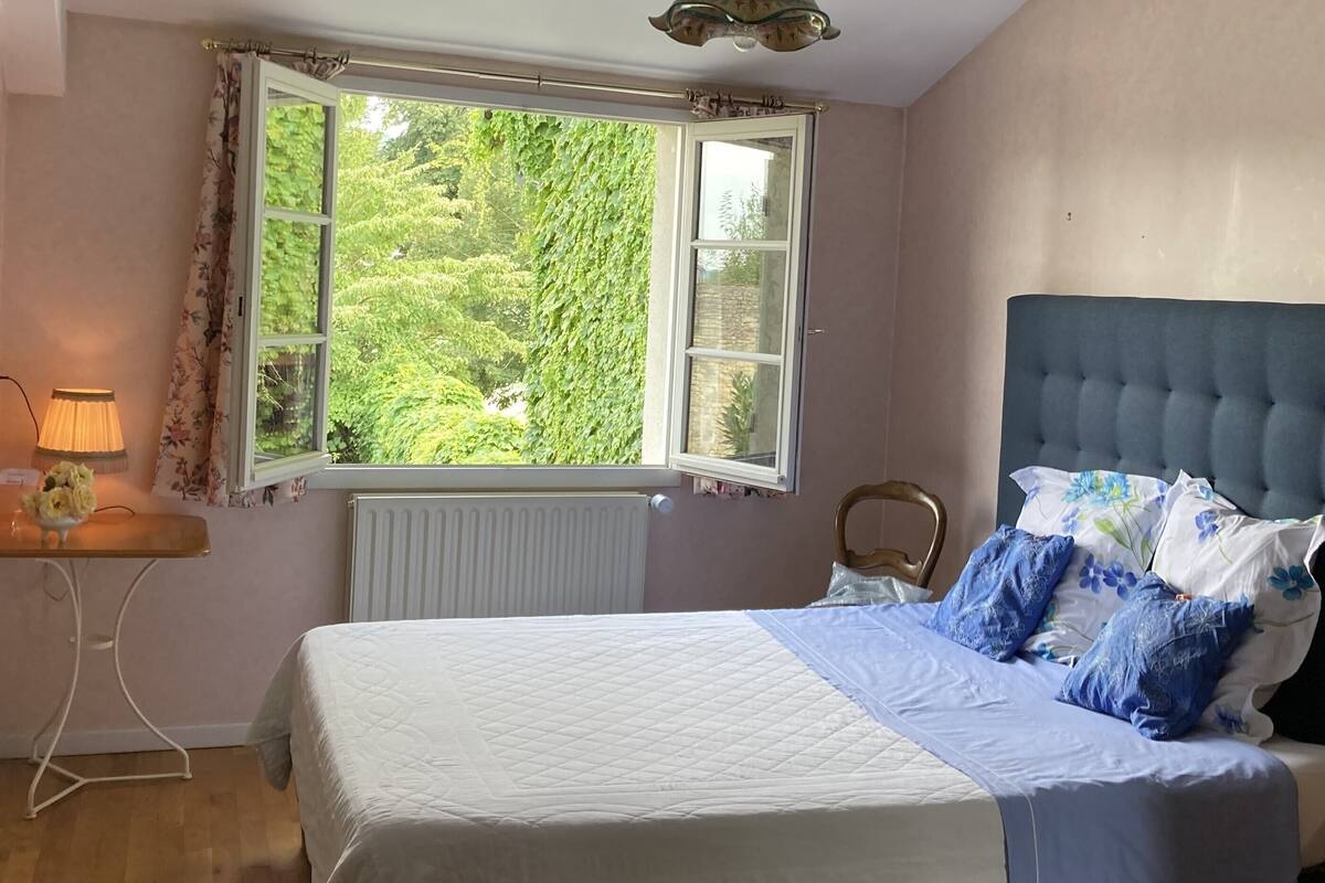 A bedroom with a large window, a bed with floral bedding, a bedside lamp, and a radiator.