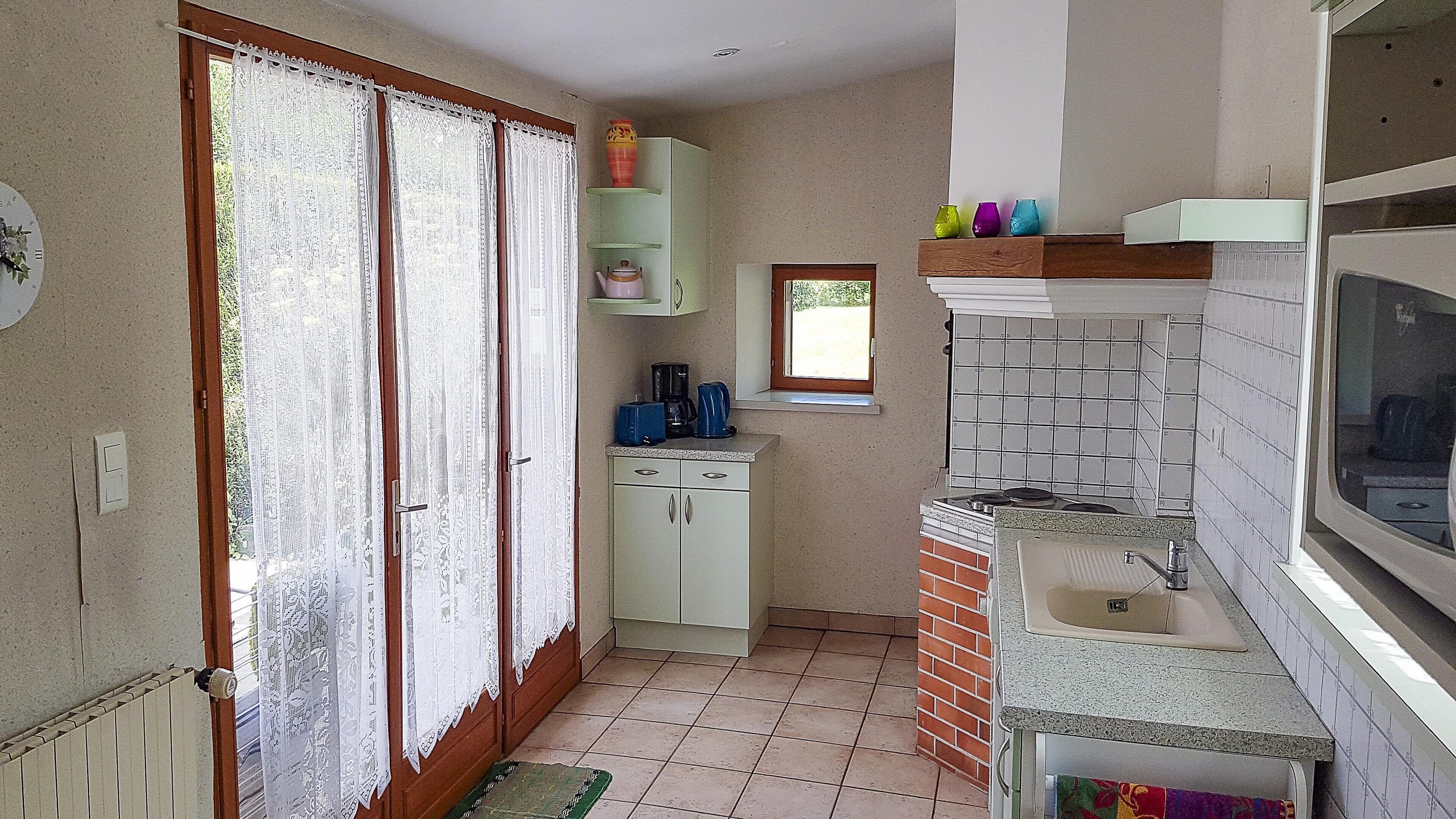 Une cuisine de taille réduite, dotée d’une fenêtre, d’un évier et d’une cuisinière. Une petite fenêtre offre une vue sur la verdure environnante.