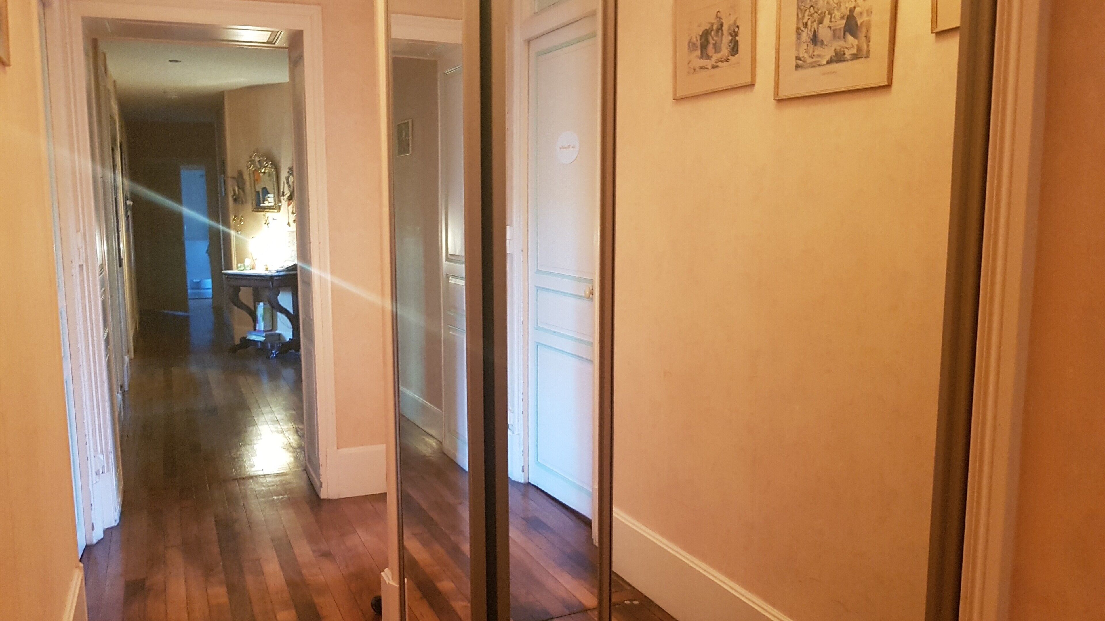 Un pasillo con suelo de madera, una puerta blanca y una pequeña mesa con lámpara.