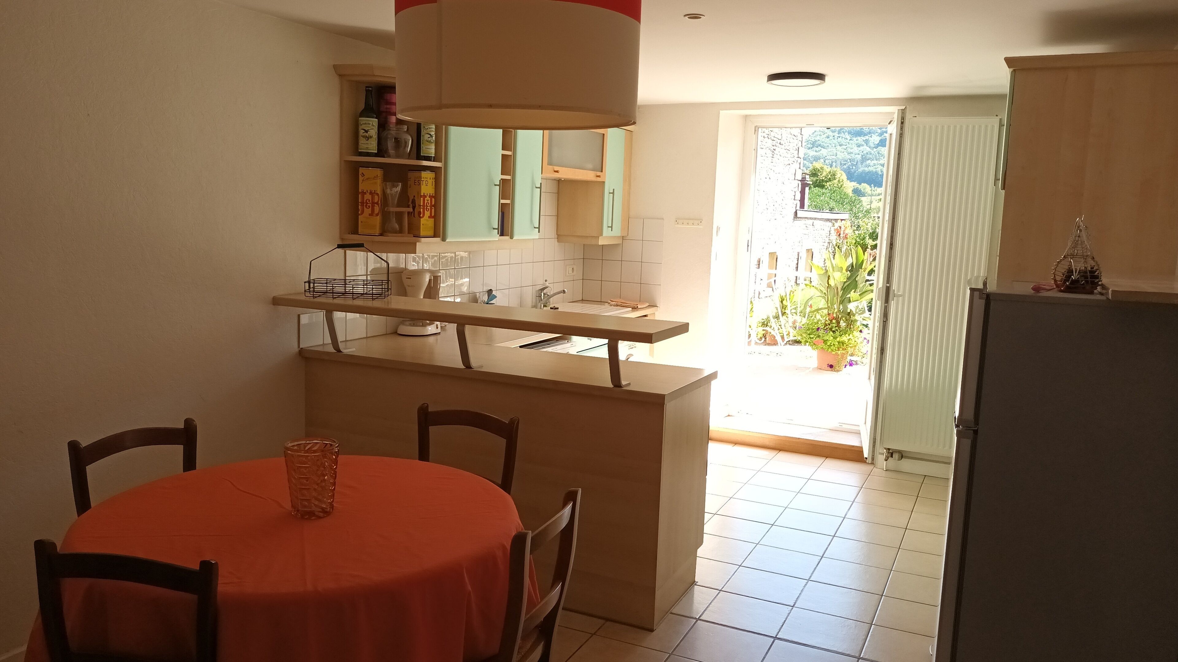 Cozinha compacta com área de refeições, destacando uma ilha pequena, cadeiras e uma mesa com toalha vermelha.