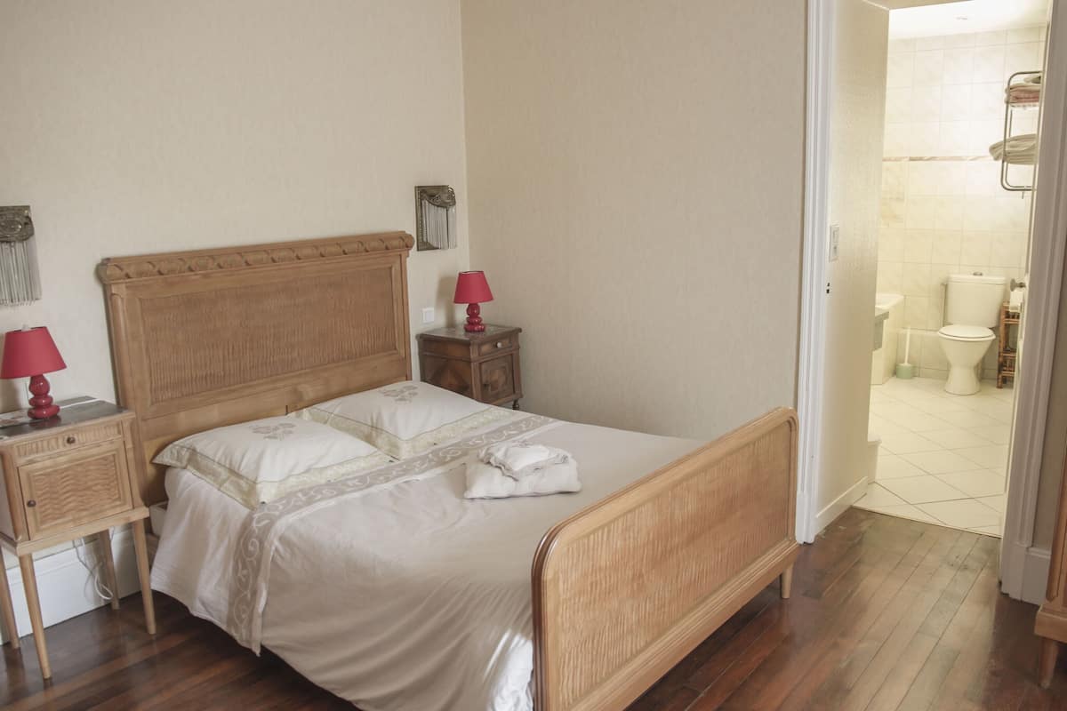 A bedroom with a wooden bed, two bedside tables, a nightstand, and a red lamp.