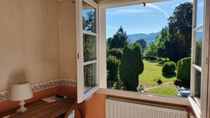 Quarto com vista para um jardim, janela com vista para o jardim, mesa com abajur e radiador.