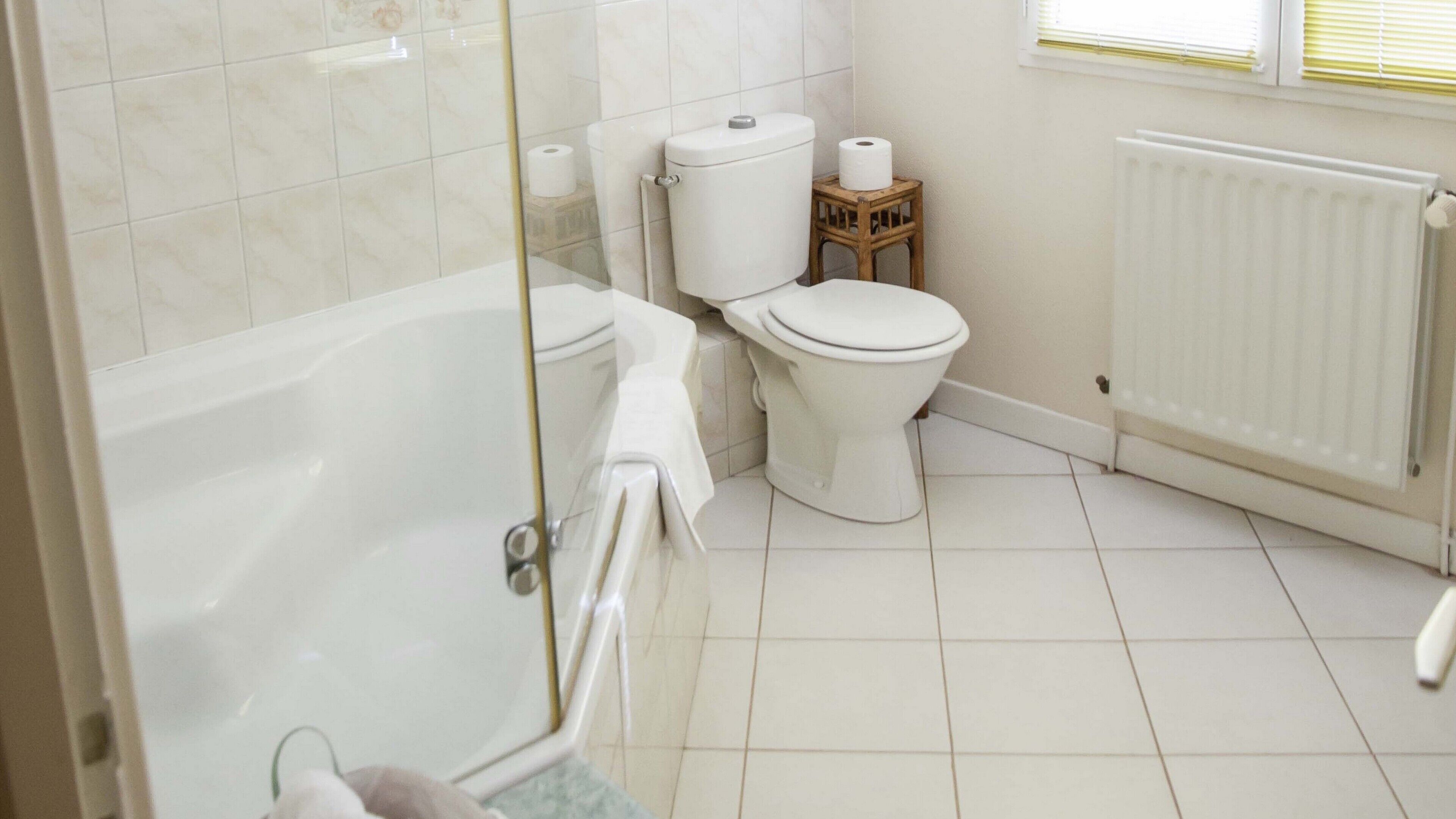 Un baño con bañera, inodoro y un pequeño taburete de madera.