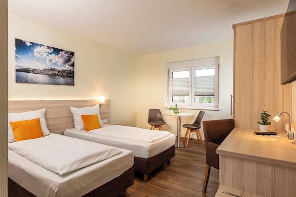Habitación de hotel con dos camas, un escritorio pequeño, una silla y una ventana con persianas.