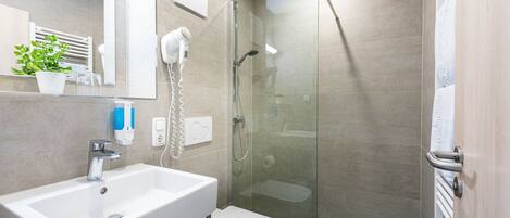 Un baño moderno con lavamanos blanco, ducha con cerramiento de vidrio y un inodoro.