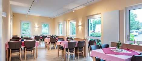 A dining area with multiple tables and chairs, large windows, and a wooden floor.