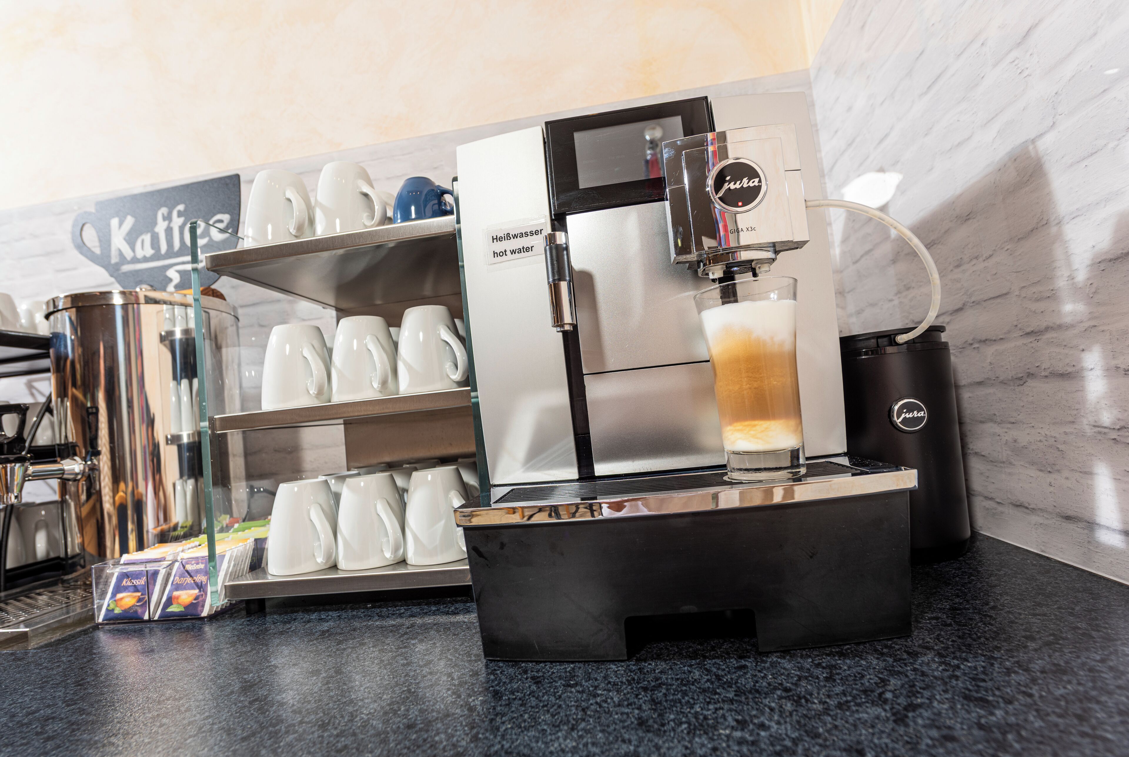 A coffee machine with a glass of hot water and a coffee machine on a counter.