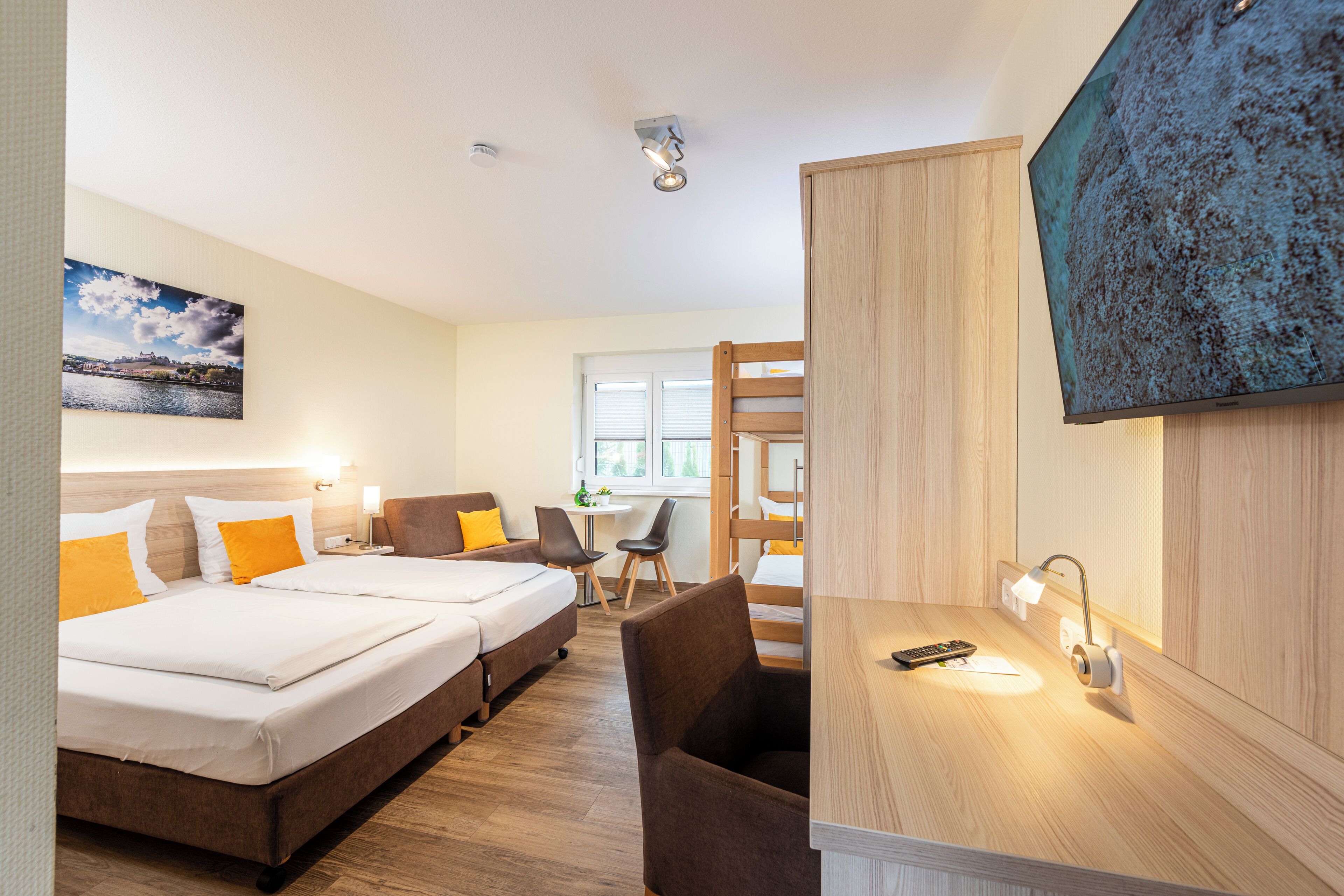 A hotel room with a bed, a desk, a chair, a TV, and a painting on the wall.