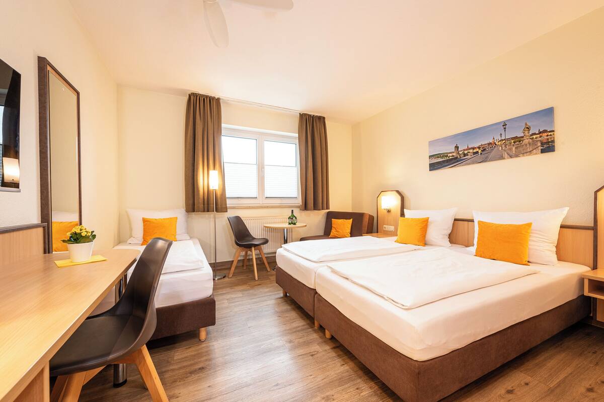 A hotel room with two beds, a desk, a chair, a small table, and a window with curtains.
