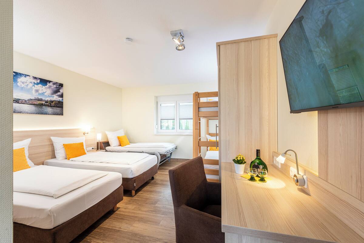 A hotel room with three beds, a wooden bunk bed, a desk with a TV, and a window.