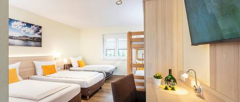Habitación de hotel con tres camas, incluida una litera de madera, un escritorio y un televisor, además de una ventana.
