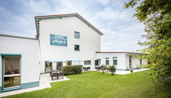 A hotel with a sign indicating 24-hour service, outdoor seating, and a well-maintained lawn. - Hotel Am Wiesenweg I 24h check-in (Hausen b. Würzburg)