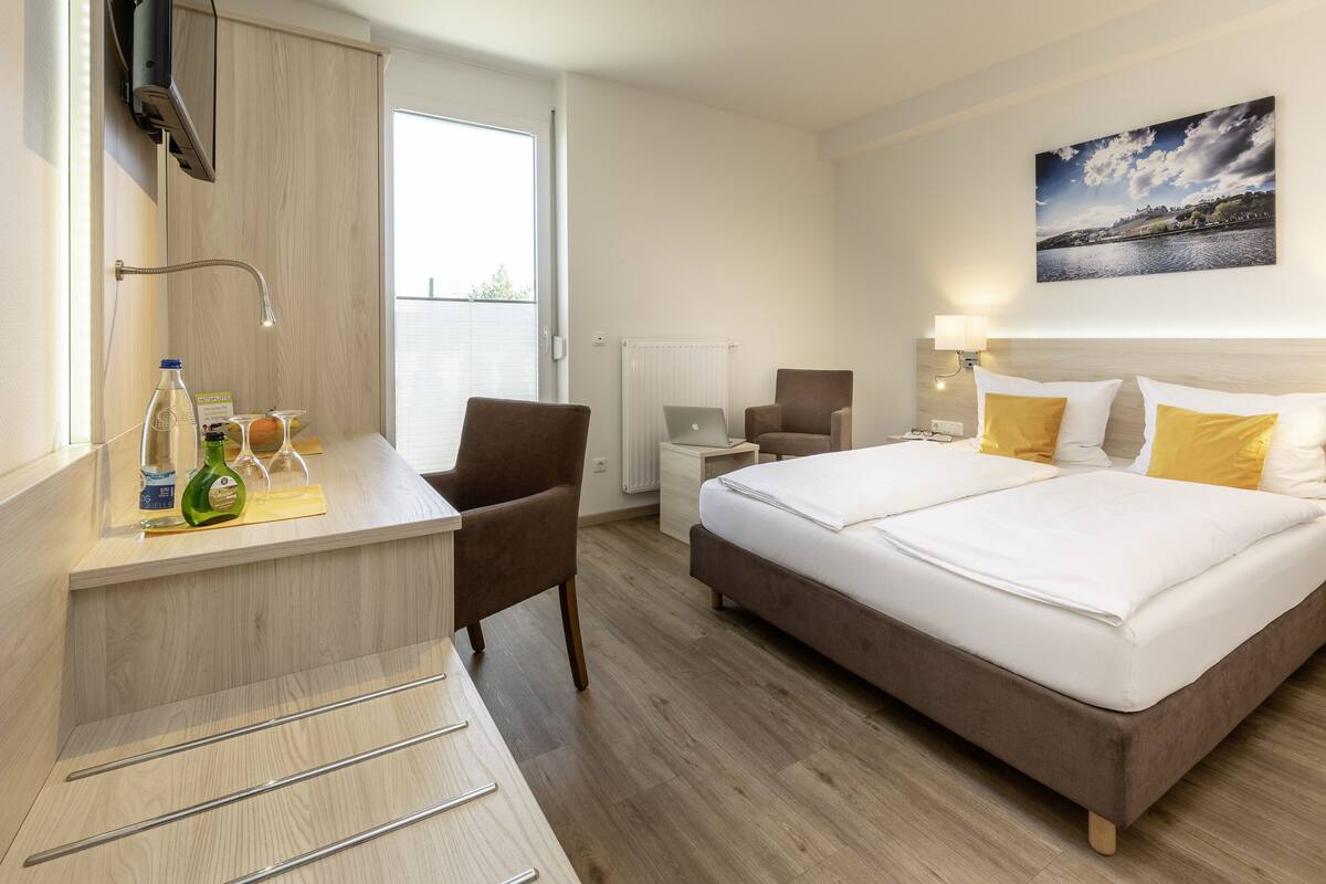 A hotel room with a bed, desk, chair, and a painting on the wall.