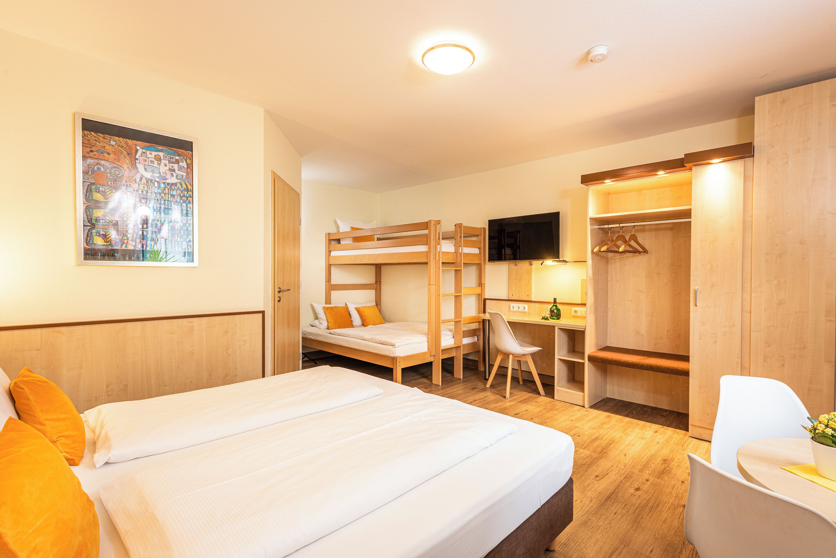 Une chambre d’hôtel avec un lit superposé, un bureau avec une chaise, une télévision et une armoire.