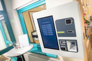 A self-service kiosk with a digital screen displaying multiple language options and a date. - Hotel Am Wiesenweg I 24h check-in (Hausen b. Würzburg)