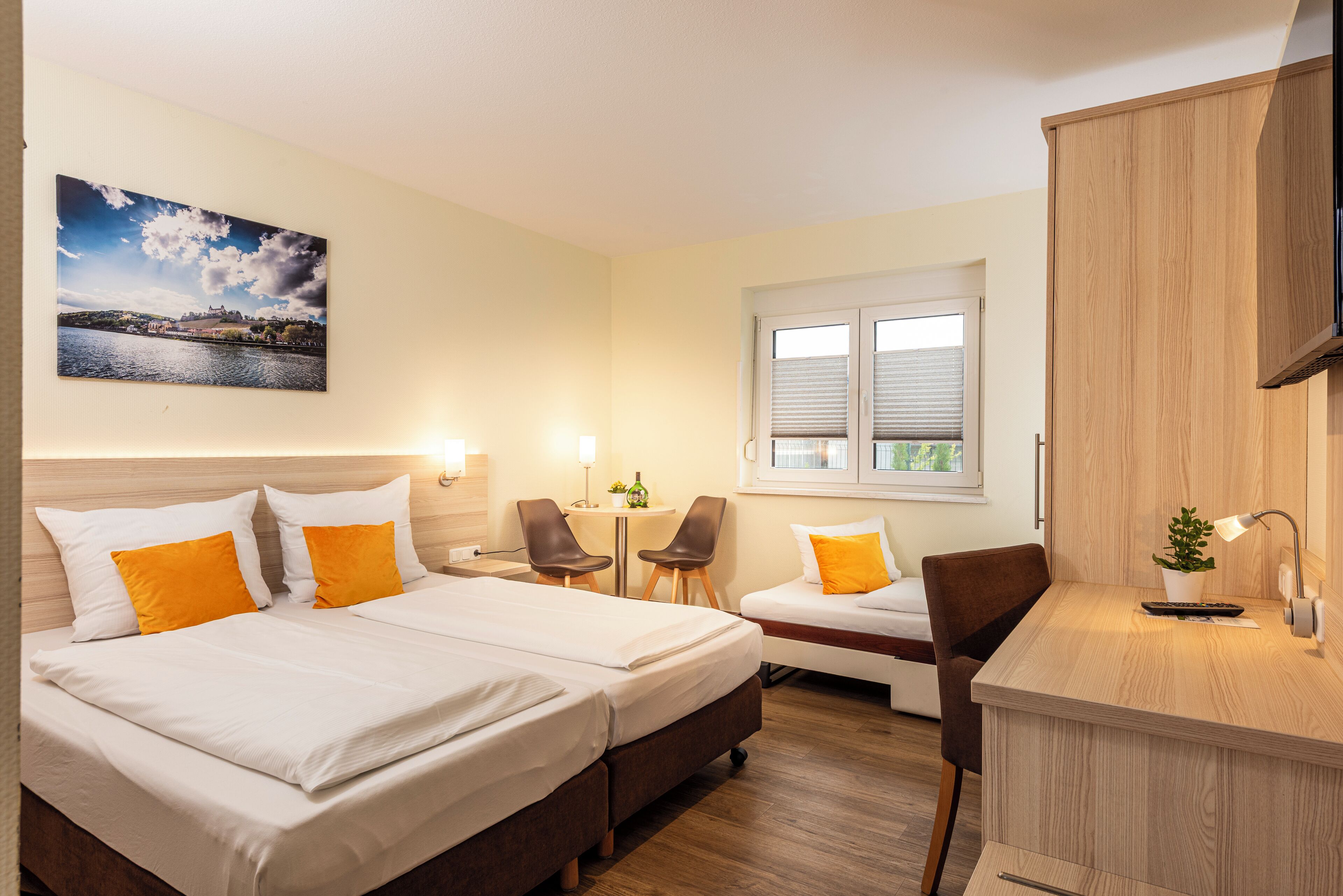 A hotel room with two beds, a desk, a chair, a small table, and a window with blinds.