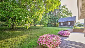 Een verzorgde tuin met een houten terras, een landelijk gebouw en weelderig groen.
