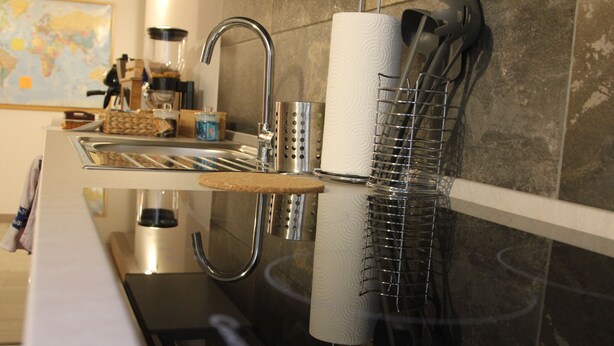 A kitchen with a stainless steel sink, a coffee maker, a paper towel holder, and a metal rack. - Sesta Strada guesthouse (Civitavecchia)
