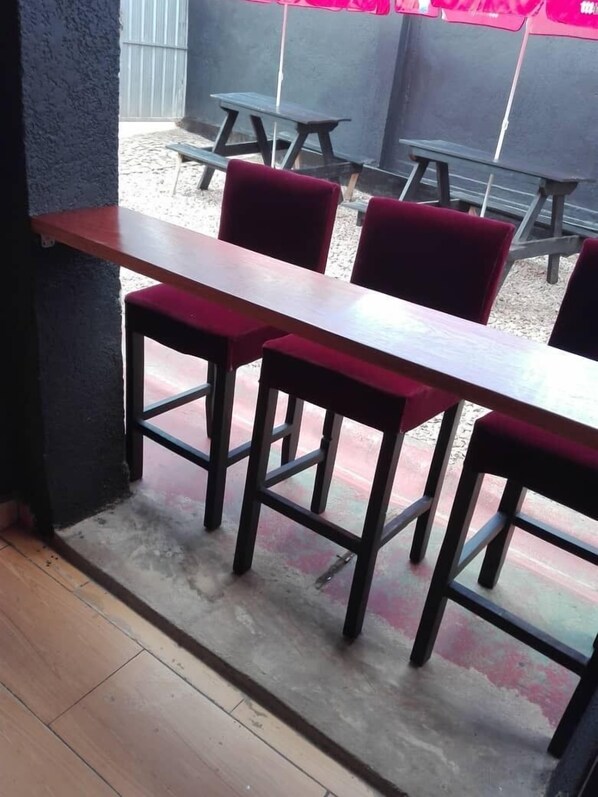 Un petit espace extérieur aménagé avec une table en bois et des chaises à l’assise rembourrée de tissu rouge.