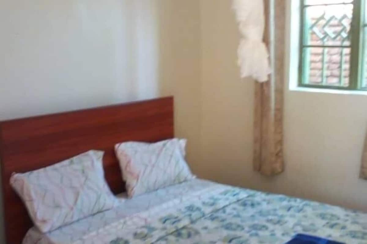 Un lit simple avec une tête de lit en bois, une moustiquaire au-dessus et une couvre-lit à motifs.