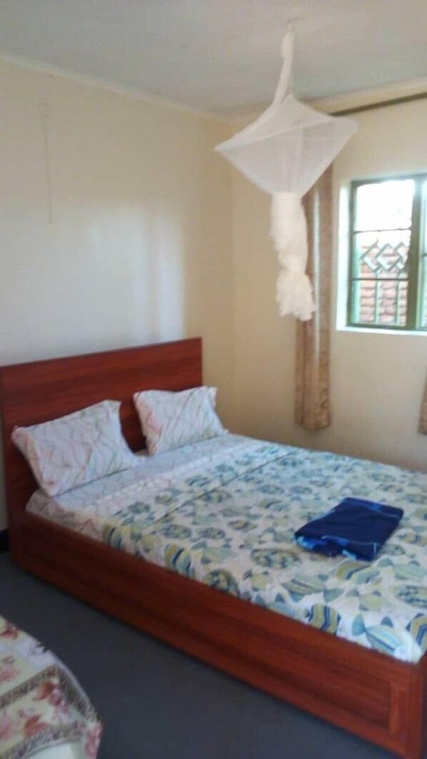 A single bed with a wooden headboard, a mosquito net above, and a patterned bedspread. - Murugo Apartment (Kigali)