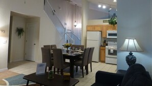 Un comedor con una mesa dispuesta para cuatro, una escalera, una cocina con electrodomésticos y un ventilador de techo.