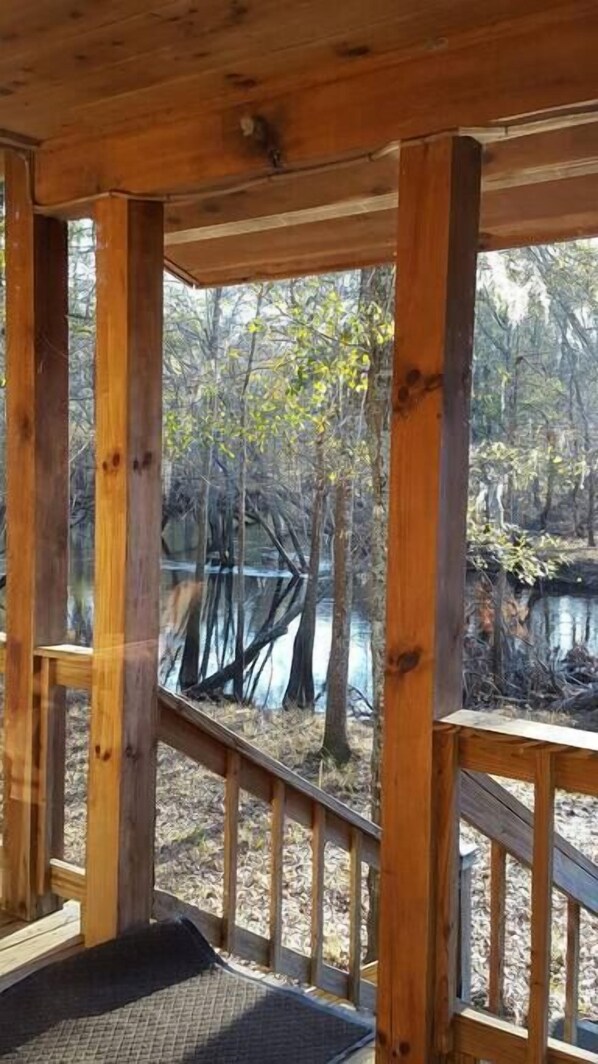 A wooden deck with a view of a forest and a body of water. - The Log Cabin on the Canoochee River (Evans County)