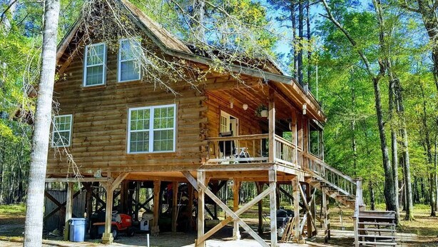 A wooden cabin with a porch and a covered deck, surrounded by trees. - The Log Cabin on the Canoochee River (Evans County)