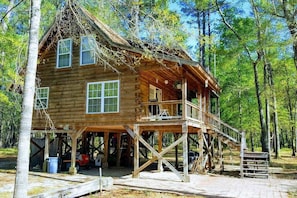 A wooden cabin with a porch and a covered deck, surrounded by trees. - The Log Cabin on the Canoochee River (Evans County)