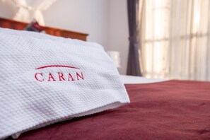 Una toalla blanca con la palabra "CARAN" bordada en rojo, sobre un cubrecolchón rojo.