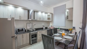 Una cocina moderna con electrodomésticos de acero inoxidable, un comedor con mesa para dos personas y un amplio ventanal con cortinas.
