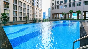 A swimming pool surrounded by high-rise buildings with balconies, a clear sky, and a sign for 'SAGOT'. - Blue Fingers Saigon Royal - Tresor (Ho Chi Minh City)