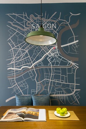 A dining area with a map mural, a table with a book and apples, and a hanging green pendant light.