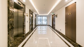 A modern hotel corridor with marble flooring, elevators, and a large window at the end. - Blue Fingers Saigon Royal - Tresor (Ho Chi Minh City)