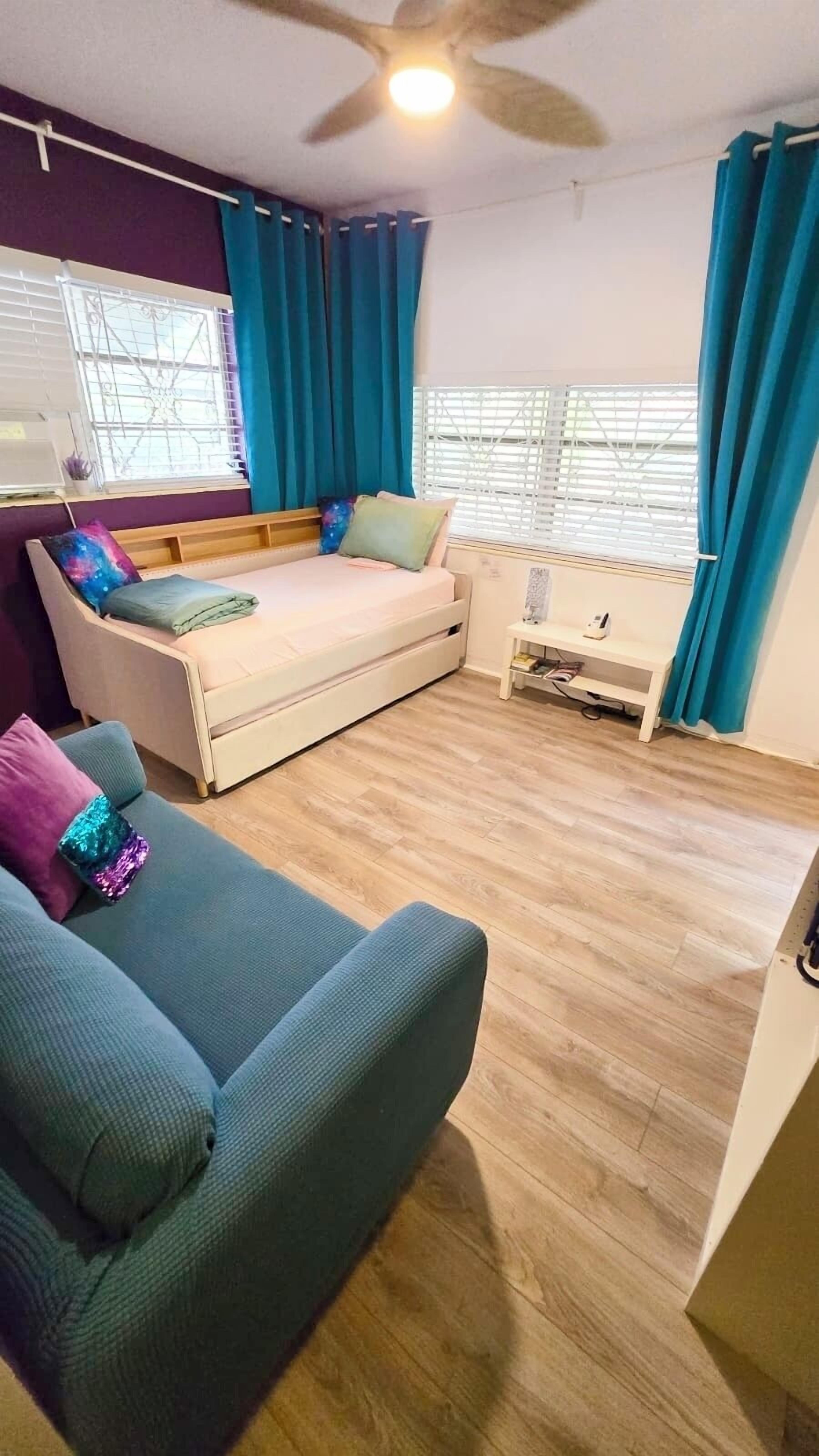 A bedroom with a bed, a sofa, a small table, and a ceiling fan.