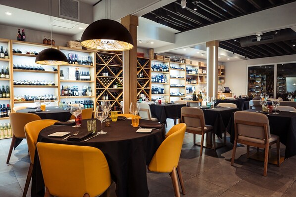 Un restaurante con mesas redondas, sillas amarillas y botellas de vino en estantes.