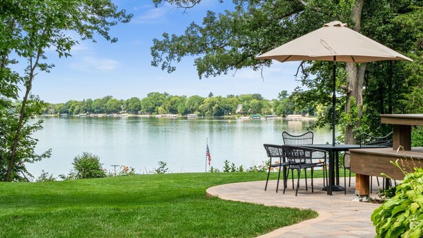 A patio with a table and chairs, an umbrella, and a view of a lake surrounded by trees. - Lake Home, salt water hot tub, sauna, boat rental (Forest Lake)