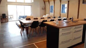 A spacious dining area with a long table and chairs, a wooden island with a sink, and large windows providing natural light. - Gite le Marquès in Aubrac with spa (Saint-Chély-d'Aubrac)