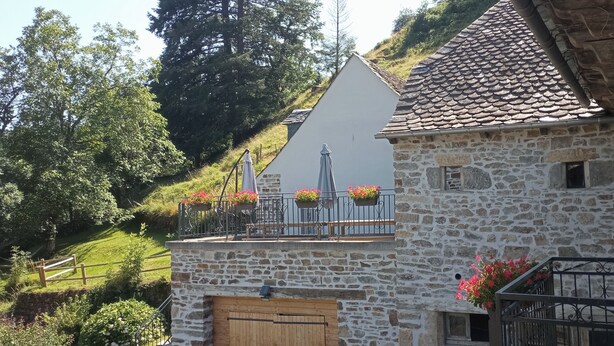 A stone building with a sloped roof, a wooden door, and a balcony with flower pots. - Gite le Marquès in Aubrac with spa (Saint-Chély-d'Aubrac)