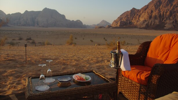 A desert view with a wicker table set with plates, glasses, and a bottle. - Sahara Rum Glamping (Wadi Rum)