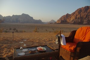A desert view with a wicker table set with plates, glasses, and a bottle. - Sahara Rum Glamping (Wadi Rum)
