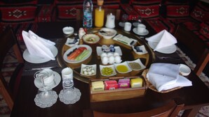 A dining table set with various dishes, including fruits, vegetables, and condiments. - Sahara Rum Glamping (Wadi Rum)
