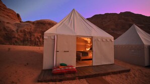 A tent with an open door revealing a bed and a small table with a cushion. - Sahara Rum Glamping (Wadi Rum)