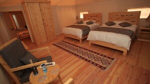 A tented accommodation with two beds, a wooden wardrobe, a small table with a bottle and glasses, and a patterned rug. - Sahara Rum Glamping (Wadi Rum)