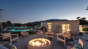 Un área de estar al aire libre con un brasero, sillones reclinables y vistas a una piscina y montañas.