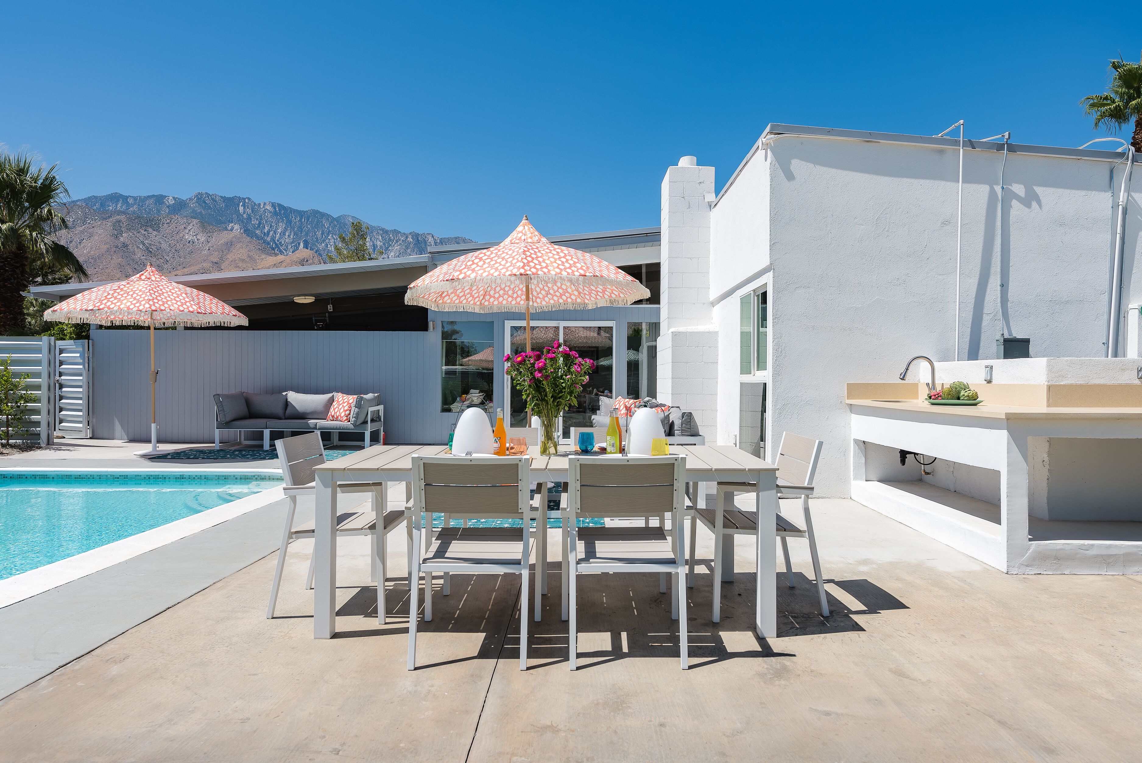 Een zwembadgedeelte met een eettafel, stoelen en twee parasols.