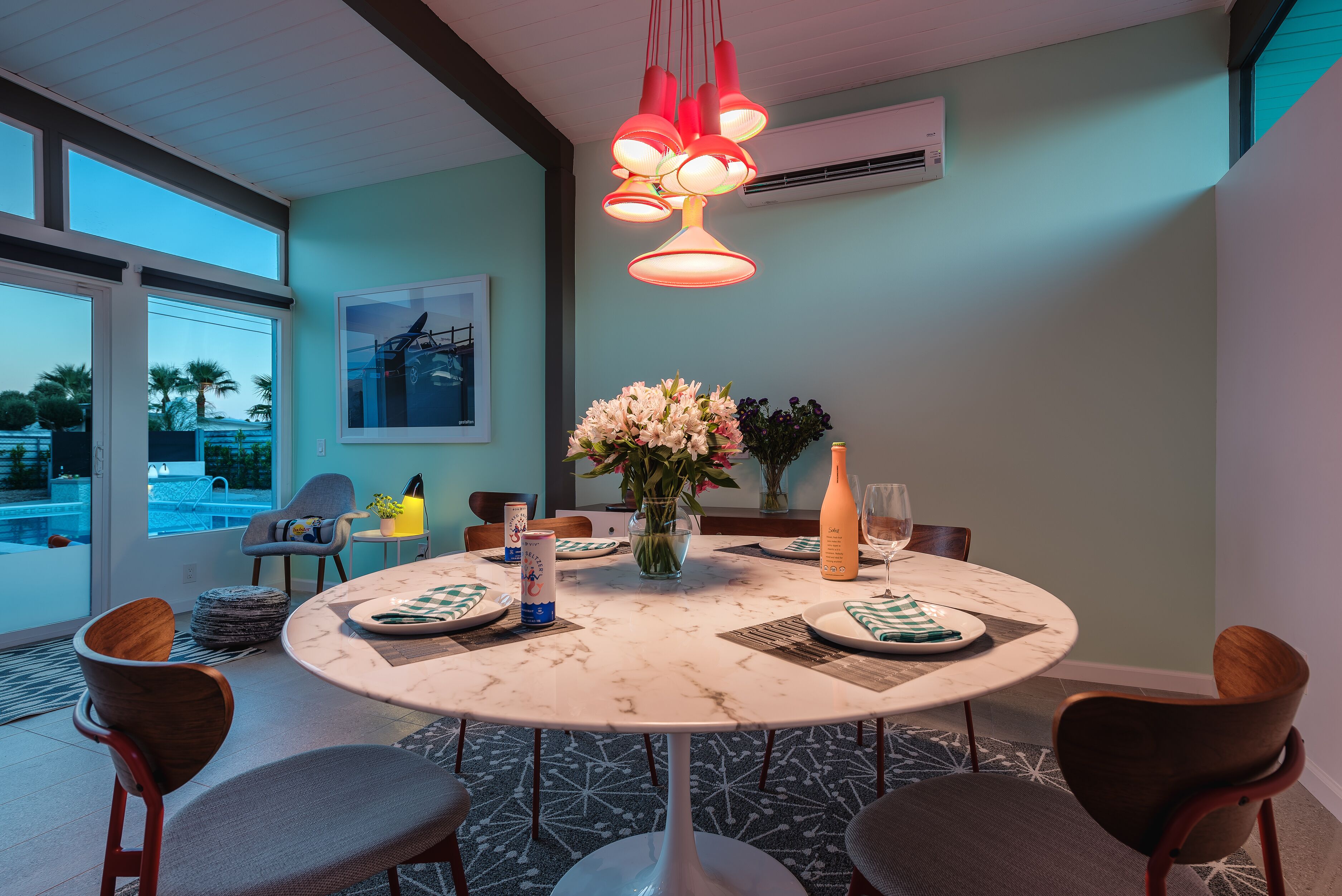 Un coin repas avec une table ronde, des chaises, un vase de fleurs et une bouteille posée sur la table.